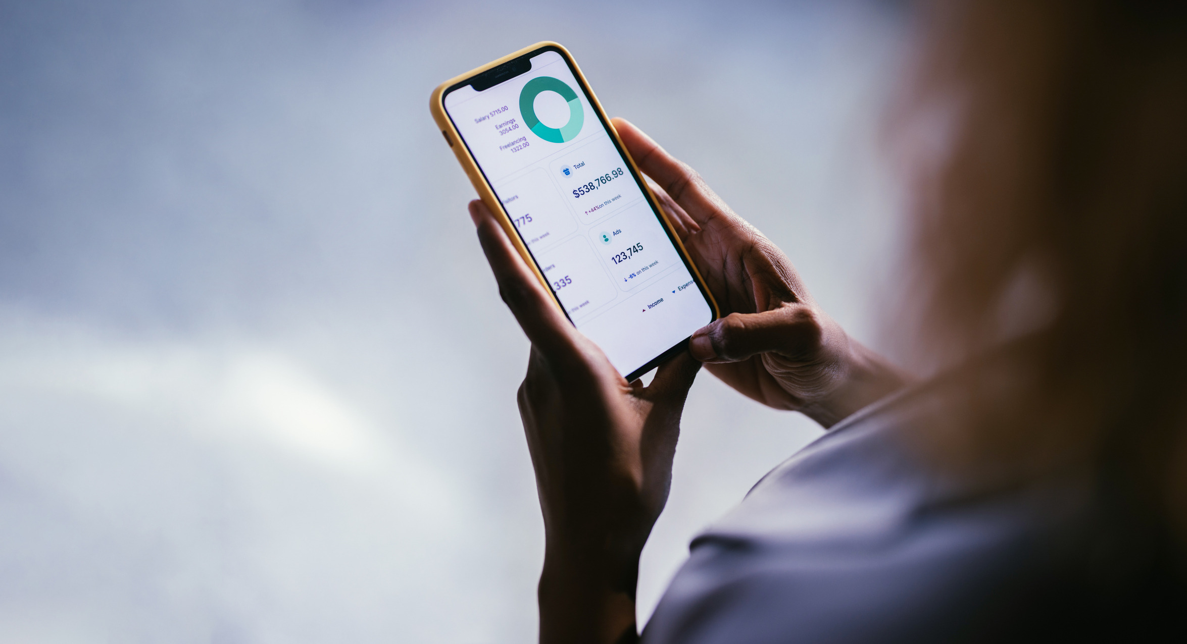 Close-Up of Hand Using Smartphone with Financial Data App A person holding a smartphone displaying financial data with charts and numbers. The image captures a modern and technological approach to personal finance management.