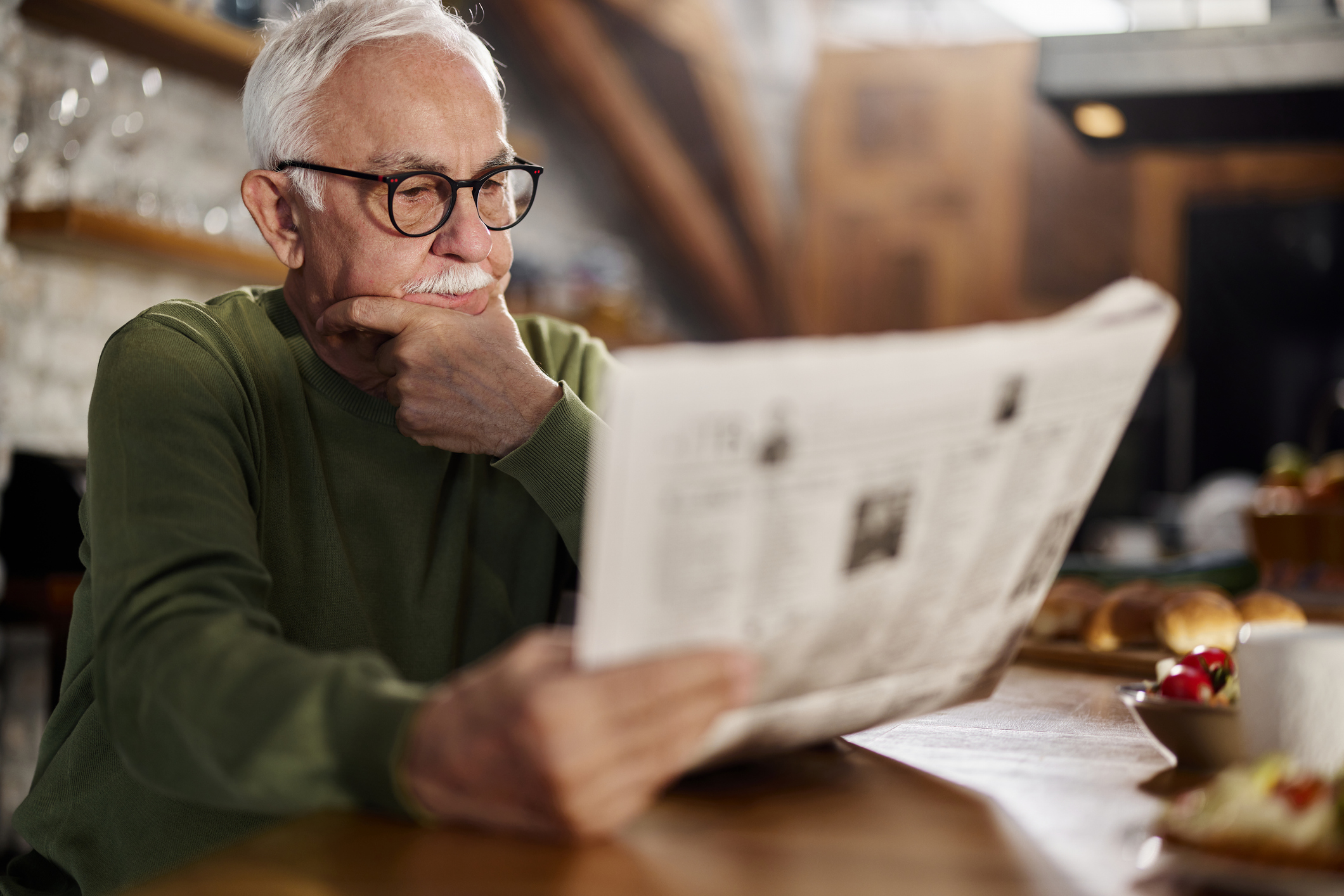 Mature man brainstorming while reading newspapers during morning time at home.